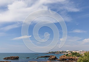 Sea surface of Biscay Bay, rocks formed by it, the Biarritz coastal line with a lighthouse.Â Biarritz, French Basque Country